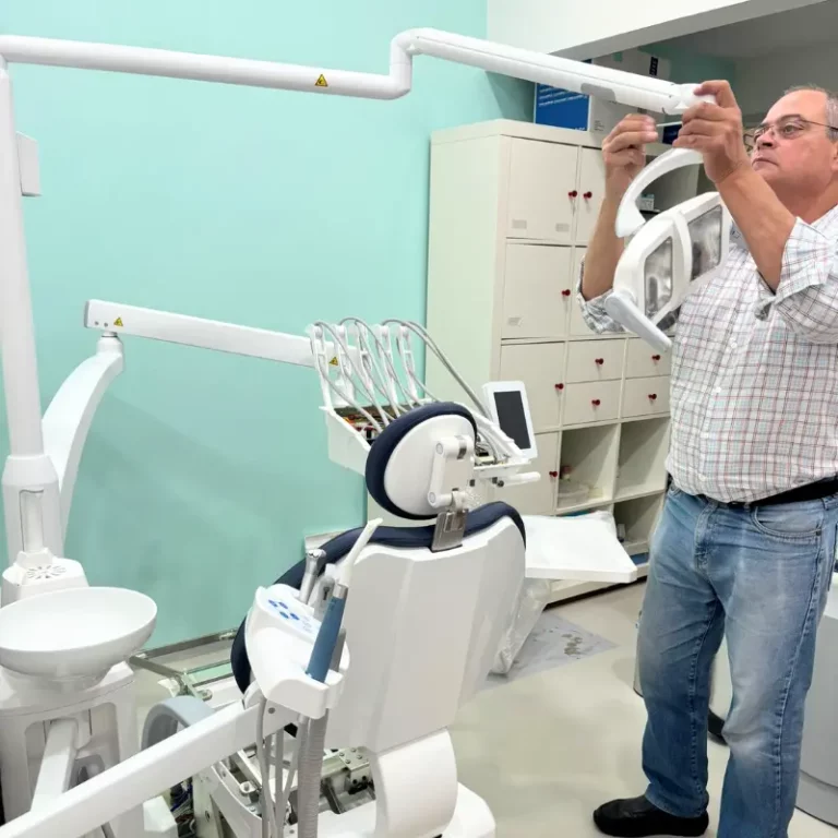 Man adjusting a dental overhead light in a modern clinic with teal walls and equipment nearby.