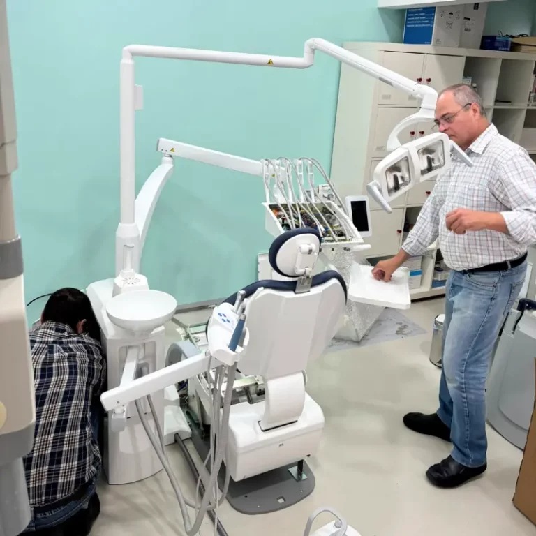 Modern dental operatory with a patient in the chair and a clinician standing nearby among multiple dental instruments and overhead lights.