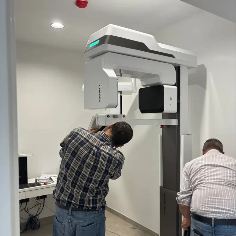 Two technicians adjust a patient under a large radiotherapy linear accelerator in a clean clinic room.